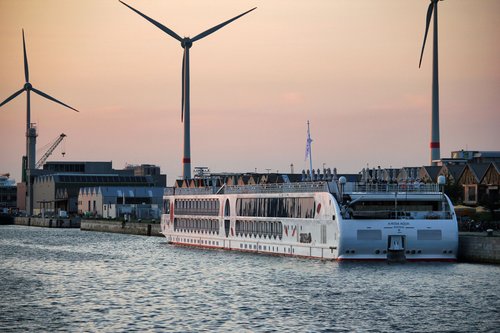 Die A-ROSA AQUA am Hafen von Antwerpen bei Sonnenuntergang, mit Windrädern und Industriegebäuden im Hintergrund.