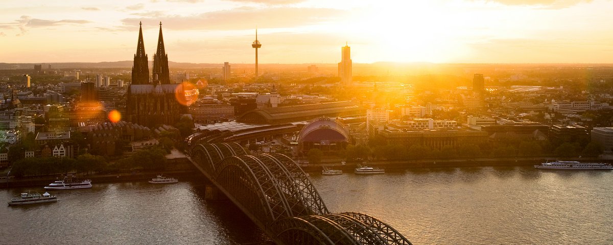 Panoramablick auf die Stadt Köln mit dem Kölner Dom bei Sonnenuntergang. Im Vordergrund die Hohenzollernbrücke, die über den Rhein führt.