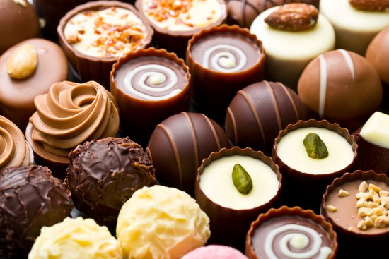 Verschiedene Pralinen in einer Schachtel, darunter weiße, dunkle und Milchschokolade, dekoriert mit Nüssen und Mustern.