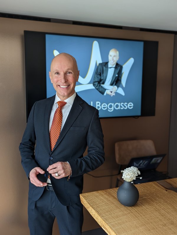 Michael Begasse steht im Anzug mit orange gestreifter Krawatte vor einem Bildschirm, auf dem seine Präsentation gezeigt wird.