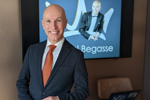 Michael Begasse steht im Anzug mit orange gestreifter Krawatte vor einem Bildschirm, auf dem seine Präsentation gezeigt wird.