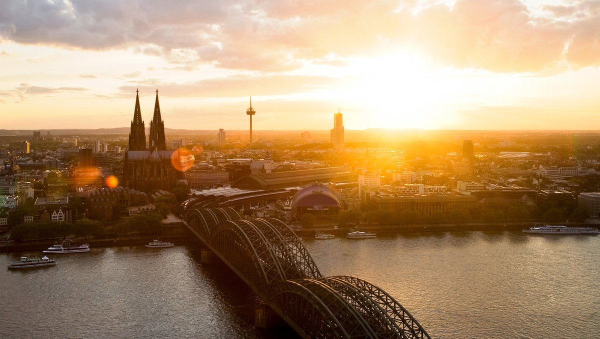 Panoramablick auf die Stadt Köln mit dem Kölner Dom bei Sonnenuntergang. Im Vordergrund die Hohenzollernbrücke, die über den Rhein führt.