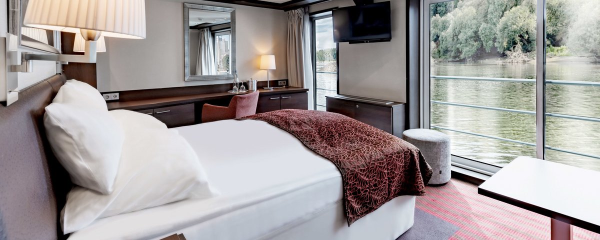 Die Juniorsuite an Bord der A-ROSA CLEA mit Doppelbett, Sitzecke, bodentiefen Fenstern und französischem Balkon.
