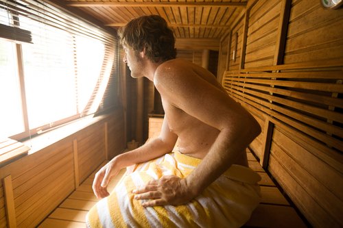 Ein Mann entspannen in der modernen Sauna mit Holzbänken und einem großen Fenster, das einen Blick auf die umliegende Natur bietet.