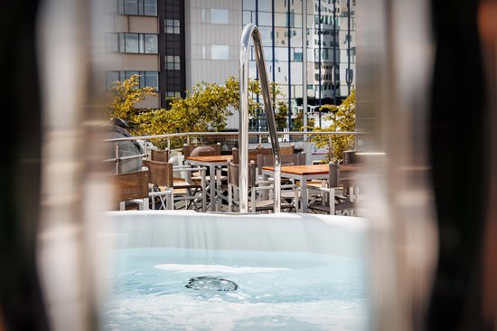 Der Whirlpool auf dem Sonnendeck bei im Sonnenlicht, im Hintergrund Sitzgruppen mit Blick auf moderne Gebäude.
