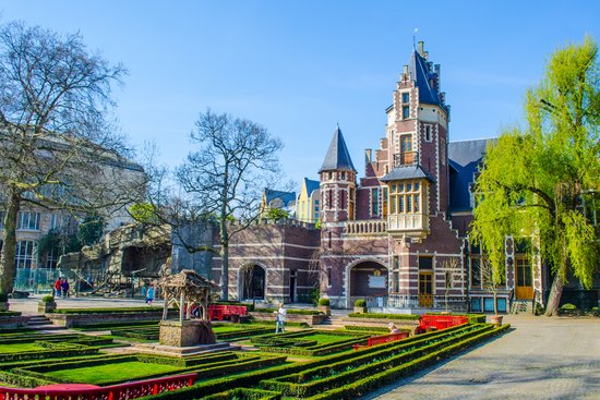 Ein historisches Gebäude im Zoo von Antwerpen, umgeben von üppigem Grün und blühenden Pflanzen, bei sonnigem Wetter.