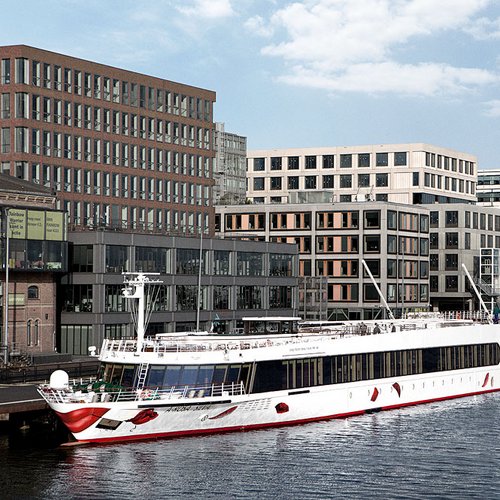 Die A-ROSA SILVA liegt tagsüber in einem Hafen vor modernen Bürogebäuden und Hochhäusern in städtischer Umgebung.