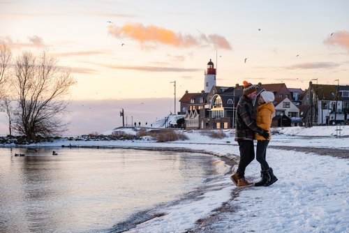 Winterliche Landschaft am IJsselmeer mit schneebedecktem Ufer und einem winterlich gekleideten Paar am Ufer, welches sich umarmt