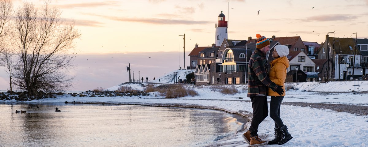 Winterliche Landschaft am IJsselmeer mit schneebedecktem Ufer und einem winterlich gekleideten Paar am Ufer, welches sich umarmt