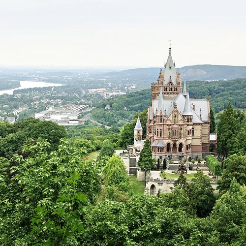 Blick auf das Schloss Drachenburg in Königswinter nahe Bonn, umgeben von üppiger Natur. Im Hintergrund Königswinter an der Donau.