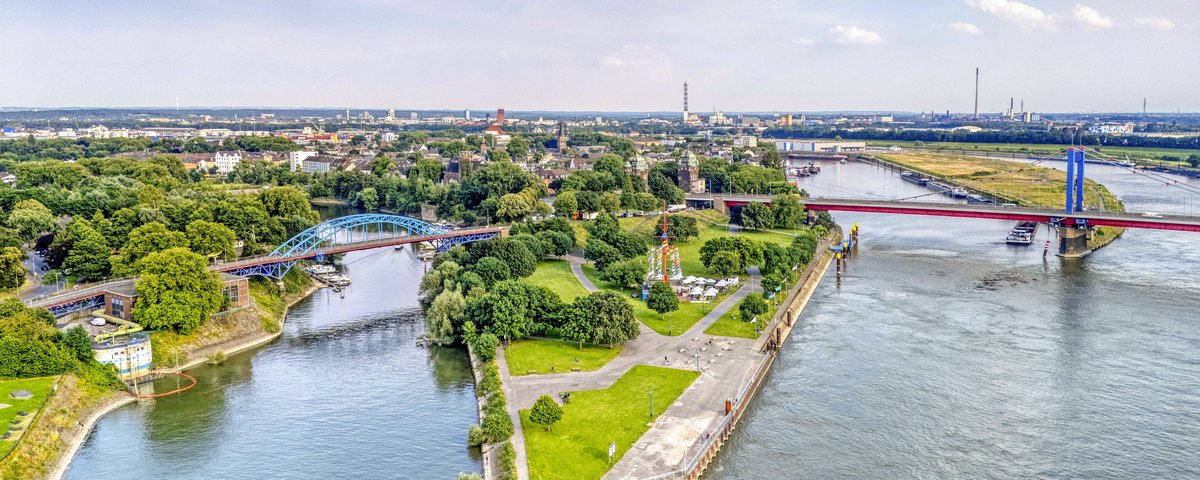 Luftaufnahme der Mercatorinsel an der Mühlenweide in Duisburg am Rhein. Wege und Grünflächen liegen zwischen Hafenbecken und Fluss, Brücken verbinden die Ufer.