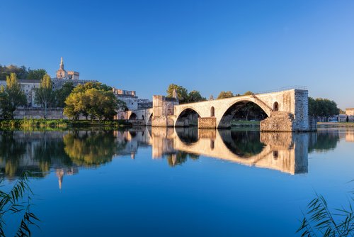 Avignon mit der berühmten Brücke Pont Saint-Bénézet über die Rhône, umgeben von historischen Gebäuden und üppigem Grün.