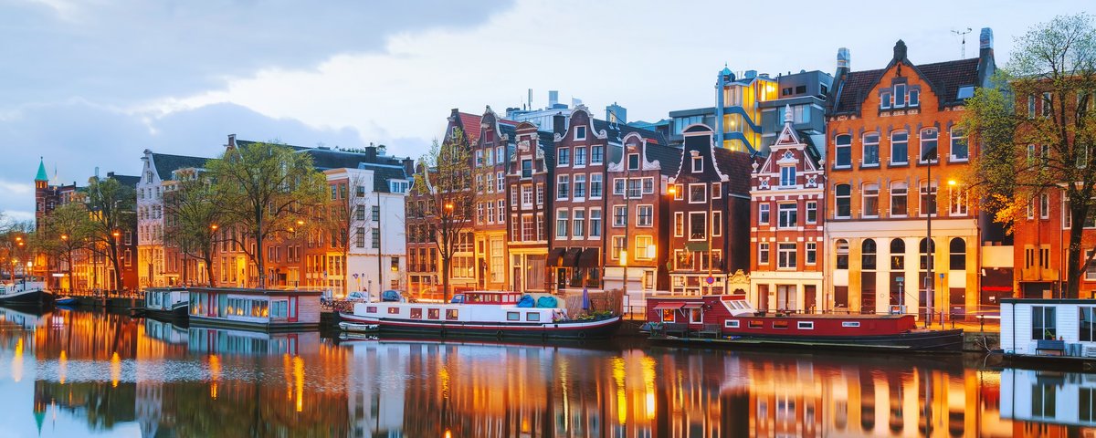Blick auf Amsterdams Grachten mit historischen Gebäuden und Booten auf dem Wasser, während der Abenddämmerung.