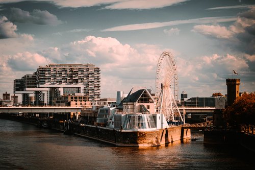 Kölner Rheinufer mit Kranhäusern, Riesenrad und historischem Turm bei bewölktem Himmel