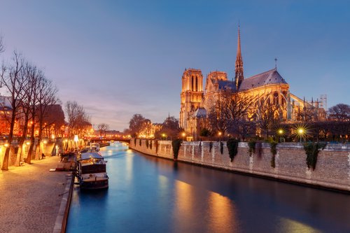 Notre Dame in Paris am Flussufer während der Abenddämmerung. Auf dem Fluss docken kleine Boote