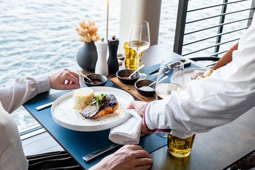 Das Restaurant SENA GRILL im industriell-modernen Design auf der A-ROSA SENA bei Tageslicht mit gedecktem Tisch und ein Teller mit gegrilltem Fisch wird gerade serviert.