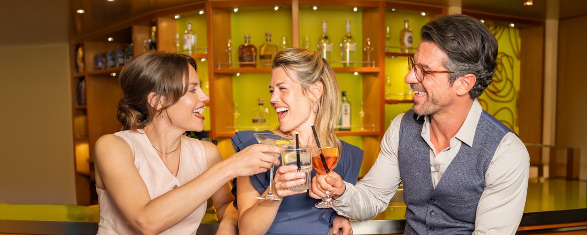 Drei Personen zwei Frauen und ein Mann sitzen an der Bar und stoßen an.