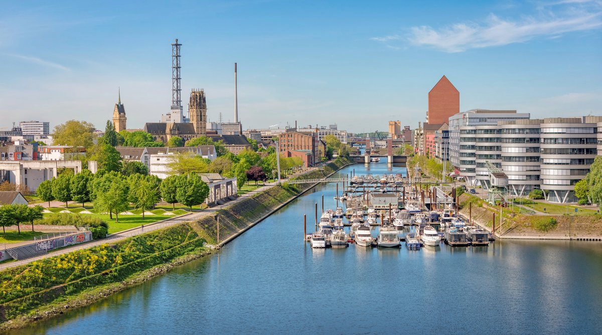 Blick auf den Innenhafen Duisburg mit Booten im Wasser, umgeben von modernen und historischen Gebäuden sowie Grünflächen