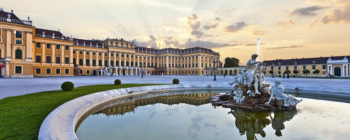 Schloss Schönbrunn in Wien bei Sonnenuntergang mit reflektierendem Brunnen und barocker Architektur