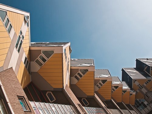 Gelbe, kubische Häuser in Rotterdam mit schrägen Wänden und Fenstern, die ineinander verschachtelt sind, vor einem blauen Himmel.